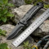 A seat belt cuuter and window breaker knife, displayed on two small rocks, next to a steel ruler.