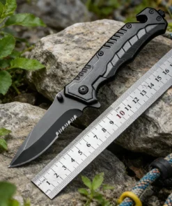 A seat belt cuuter and window breaker knife, displayed on two small rocks, next to a steel ruler.