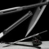 A straight, double edged dark sword leaning against a small log with its scabbrd lying below on the floor, and product highlights above.