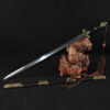 A straight double edged Chinese Jian sword leaning against a small wood log, with its scabbard below on the floor.