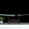 A long Nagamaki sword sheathed within its green scabbard, displayed on a wooden stand.