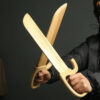 A mans arms holding two white Wing Chun training, wooden knives.