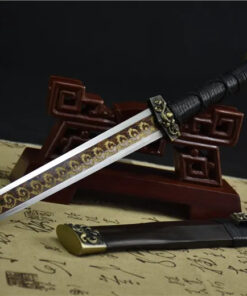 A straight, double edged decorative dagger leaning against a wood stand, with its scabbard on the floor.