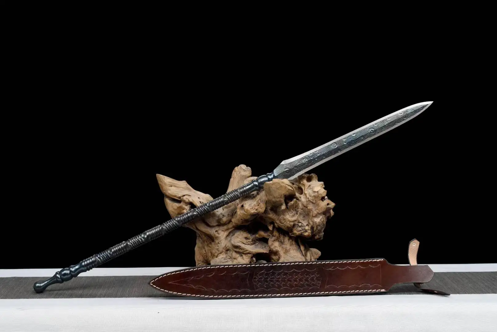 Short Spear An all-steel short spear weapon, displayed on a wood log, with its leather sheath below on the floor.