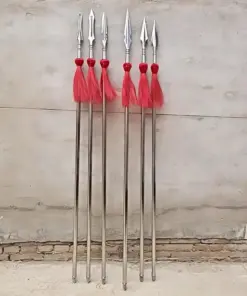 Six Wushu spear models with red-tassels, leaning against a cement wall.