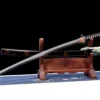 A folded steel clay tempered Katana displayed next to its scabbard, on a small sword-stand.