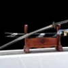 A T12A crane sword, displayed next to its decorative scabbard, on a small wooden Katana-stand.