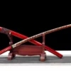 A red Katana sword and its scabbard leaning against a small wooden stand.