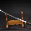 A Japanese Katana sword leaning against a wooden stand, with its brown scabbard lying below on the floor.