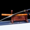 A Katana saber sword and its orange scabbard displayed on a small wooden stand.