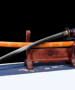 A Katana saber sword and its orange scabbard displayed on a small wooden stand.