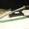 A Japanese Samurai master Katana displayed on a small wooden sword stand, with its green colored scabbard below on the floor.