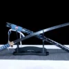 A T10 clay tempered Katana and its scabbard, displayed leaning against a small wooden sword-stand.