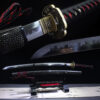 A black and red Katana sword, displayed on a wooden stand, alongside its scabbard.