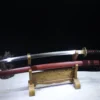 A Japanese Samurai Katana and its red colored scabbard displayed on a small wooden sword stand.