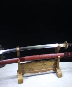A Japanese Samurai Katana and its red colored scabbard displayed on a small wooden sword stand.