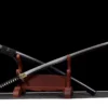 A curved Katana sword displayed crossed against its black scabbard, leaning against a small wooden sword-stand.