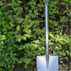 A garden shovel leaning against a garden hedge.