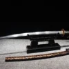 A hand forged Katana folded steel sword displayed on a wooden sword-stand, with its scabbard below on the floor.