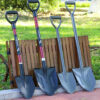 Four digging shovels of differing design, leaning against a wood turned-over outdoor table.