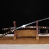 A Japanese Tachi sword displayed next to its decorative scabbard, on a small wooden sword-stand.