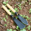 Two gardening trowels of differing design, laying side-by-side on the ground.