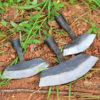 Three weed cutter tool heads of differing sizes, lying on earth ground.