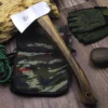 A small forest hatchet with a wood handle, displayed against a camouflage bag, on a wooden floor.