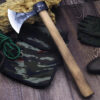 A throwing tomahawk, with a wooden axe handle, displayed against a camouflage bag on floor-boards.