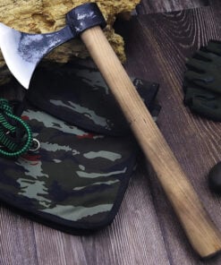 A throwing tomahawk, with a wooden axe handle, displayed against a camouflage bag on floor-boards.