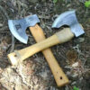 Two small hatchets displayed crossed over one-another, on a forest floor.