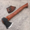 A hand forged bushcraft hatchet with a wooden handle, displayed on a concrete floor next to its small leather axe sheath.