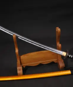 A Iaido blunt Katana sword displayed on a wooden stand, with its orange colored scabbard below on the floor.