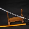 A Iaido Katana displayed on a wooden sword stand, with its orange colored scabbard below on the floor.