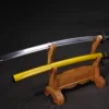 A Japanese Samurai Katana and its yellow colored scabbard displayed on a small wooden sword stand.