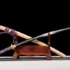 A sharpened Katana saber sword displayed crossed against its wooden scabbard, leaning against a small wood sword-stand.