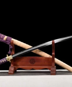 A sharpened Katana saber sword displayed crossed against its wooden scabbard, leaning against a small wood sword-stand.