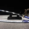 A sky blue Katana leaning against a small wooden sword stand, with its scabbard lying below on the floor.