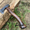 A woodsman hatchet with a wooden handle displayed against a log, on the ground.