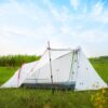 A white colored, small 1.5 person tent displayed with its entry door opened, erected in a grass field.