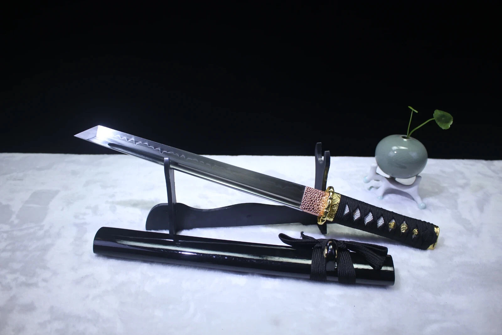 Black Tanto Knife A black Tanto knife displayed leaning against a small wooden stand, with its sheath below on the floor.