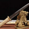 A Chinese knife with a double edged, straight blade, leaning against a small Chinese dragon statue.