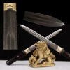 Two double edged daggers leaning against a small Chinese dragon statue, along with knife highlights above.