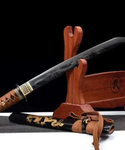 A Japanese Tanto knife with a dragon engraved blade, displayed leaning against a small wooden stand, with its sheath below on the floor.