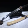 A Japanese fighting knife Tanto displayed on a small wooden stand, with its white wood scabbard below on the floor.