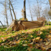 A brown colored military bivy tent erected on leaf covered grass, with trees in the background.