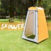 A yellow and gray colored camping shower tent, displayed erected on a grass lawn, with trees in the background.