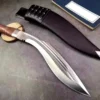 A Kukri machet survival knife lying next to its leather sheath and a small book.