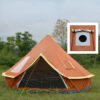 A brown orange colored round tent yurt, displayed erected in a grass field, with trees in the background.