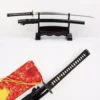 A black master sword and its black Katana scabbard displayed on a small wooden sword stand, along with a close-up of the Katana's handle and red colored sword bag below.